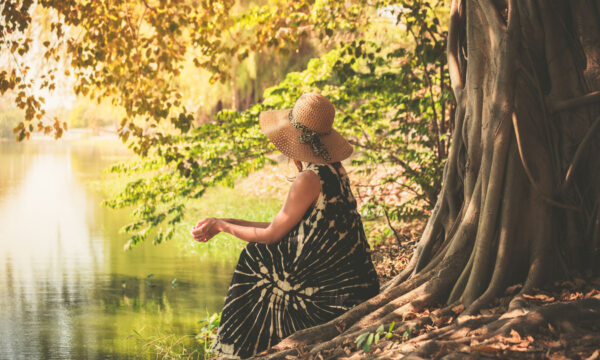 Woman sitting under tree by the river A young woman is sitting under a tree by the river